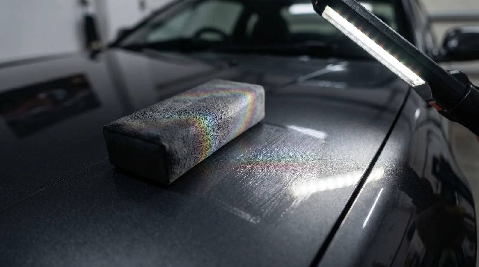 Macro close-up of the cross-hatch ceramic coating application pattern showing iridescent film on a charcoal JDM bonnet