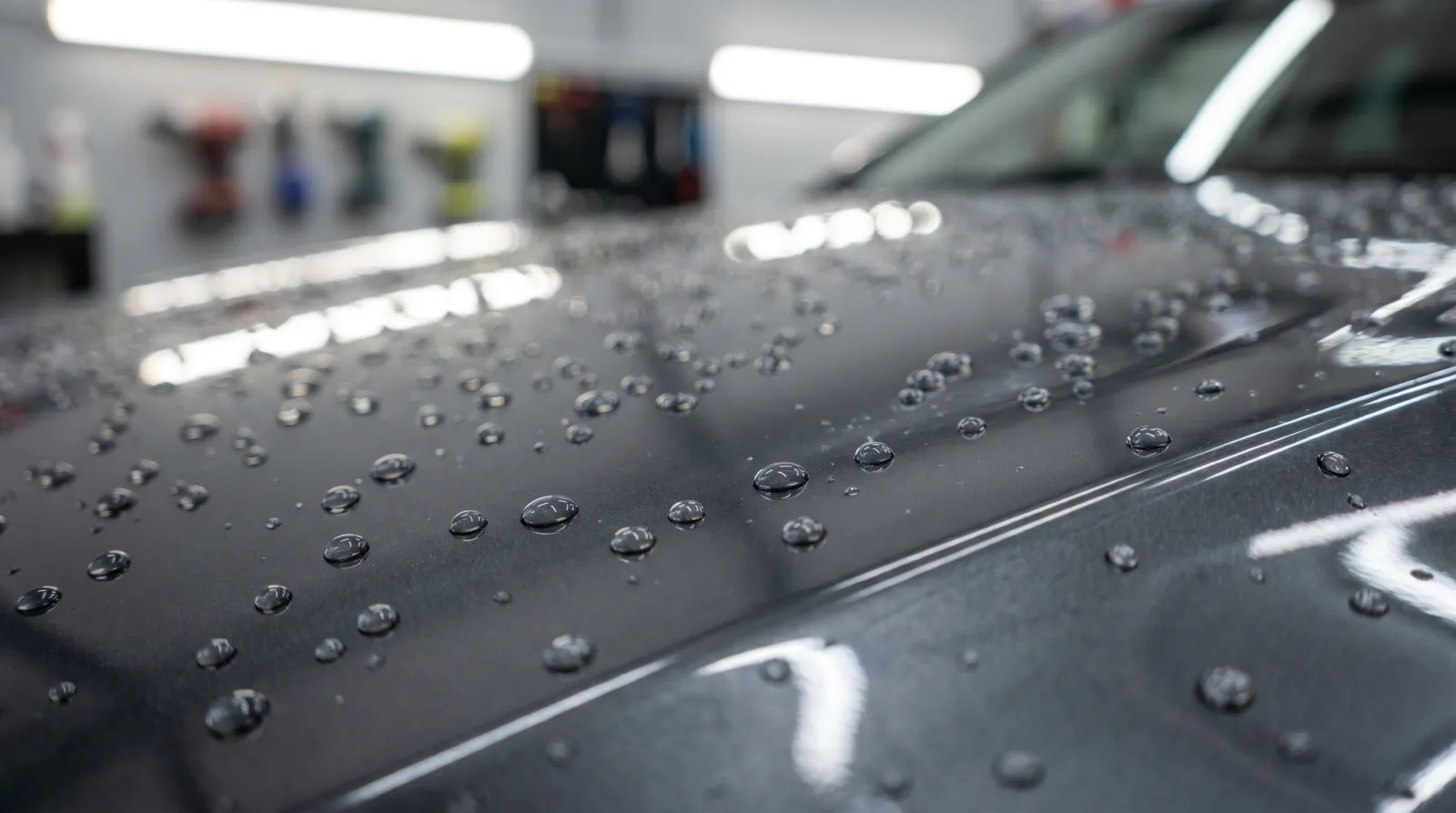 Fresh ceramic coating beading water at high contact angle on a dark charcoal JDM bonnet