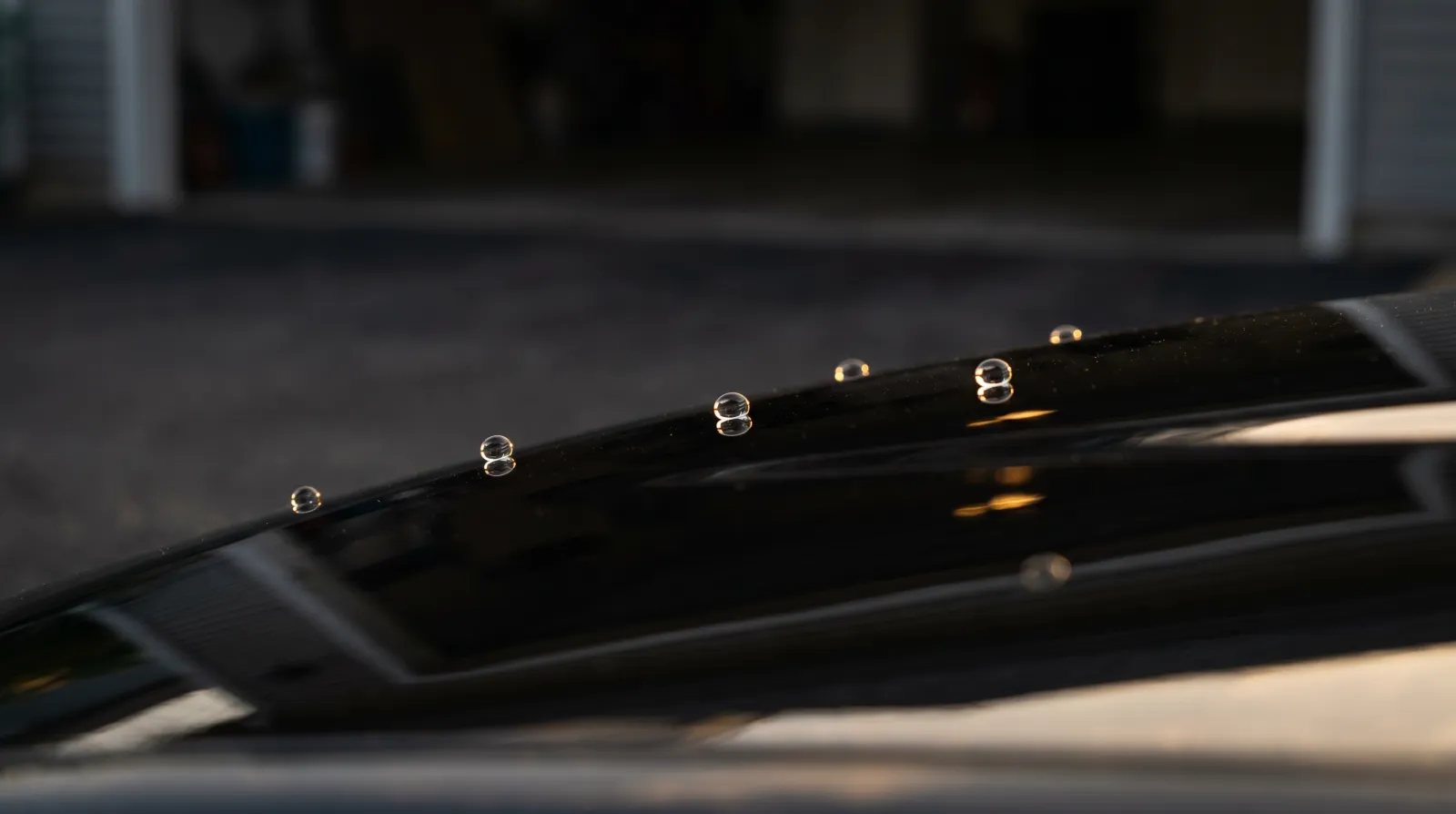 Tight water beads rolling off a glossy black ceramic-coated JDM bonnet at low angle