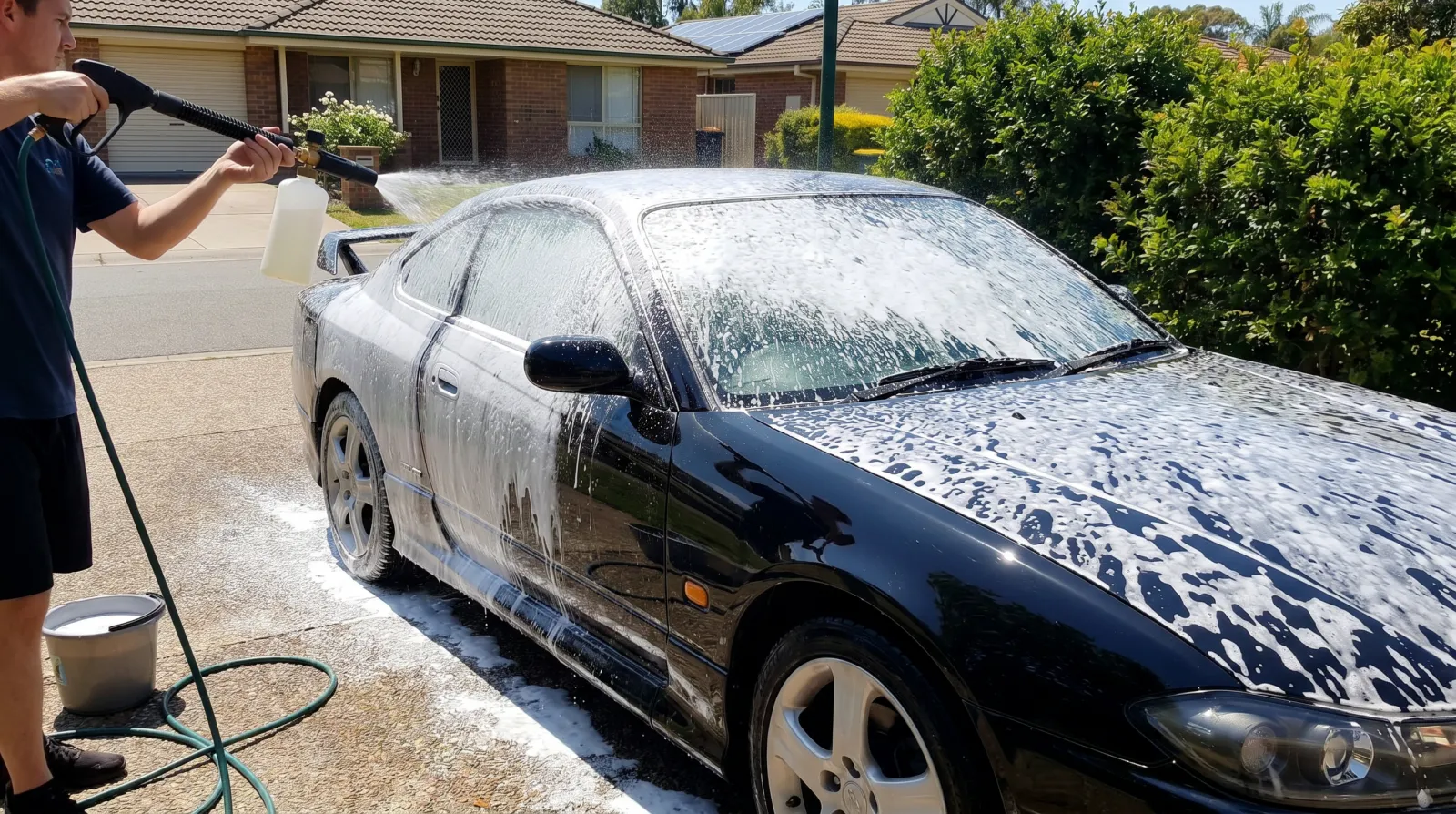 Snow foam cannon blanketing a coated coupe with thick white suds in a driveway