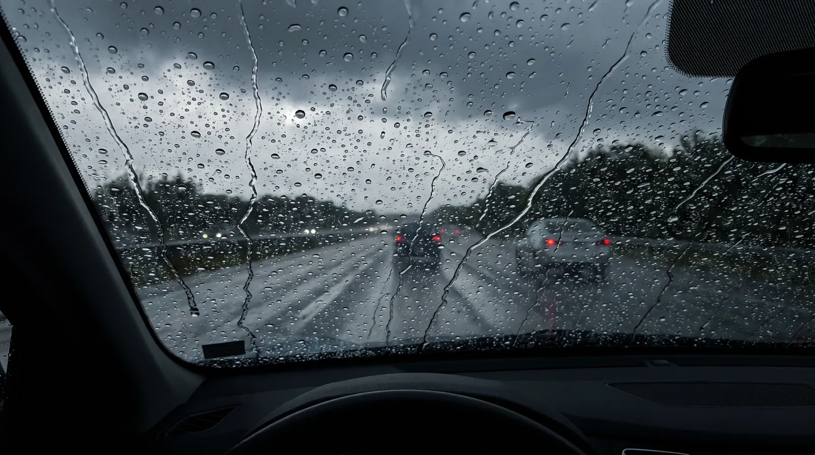 Water sheeting off a hydrophobic-coated windscreen during rain, viewed from the driver's seat
