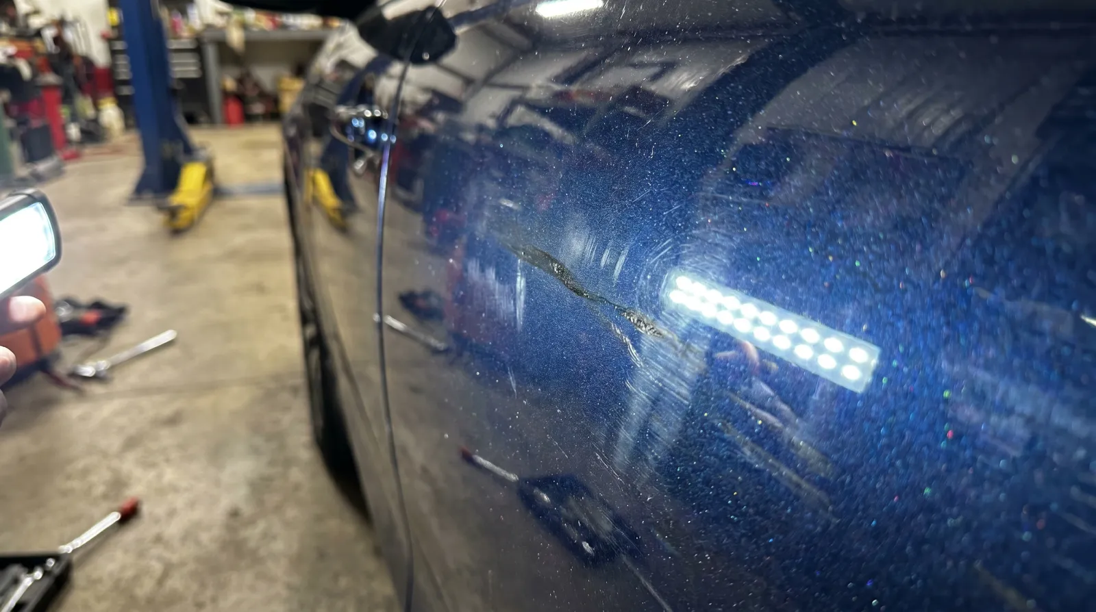 Rainbow-iridescent ceramic coating high spots on a dark blue car panel under a focused detailing light