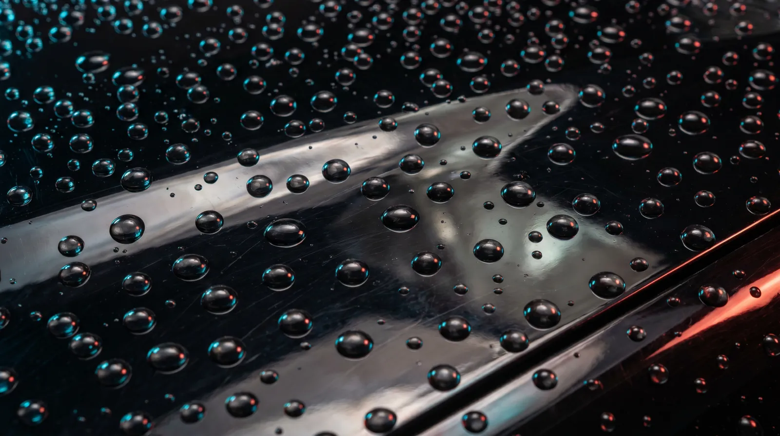 Extreme close-up of perfectly spherical water beads on a glossy black ceramic-coated panel