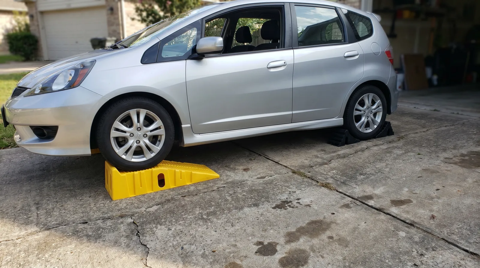 The front wheels of a hatchback resting on yellow drive-on ramps with the rear wheels chocked