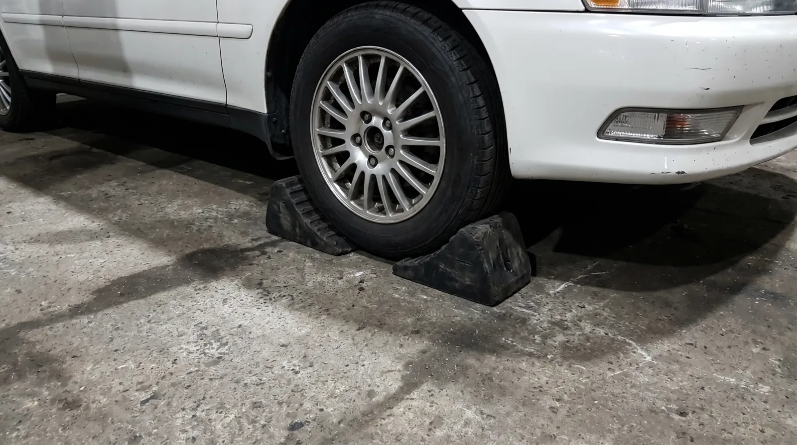 Rubber wheel chocks wedged tight against both sides of a rear tyre on a JDM sedan lifted at the front