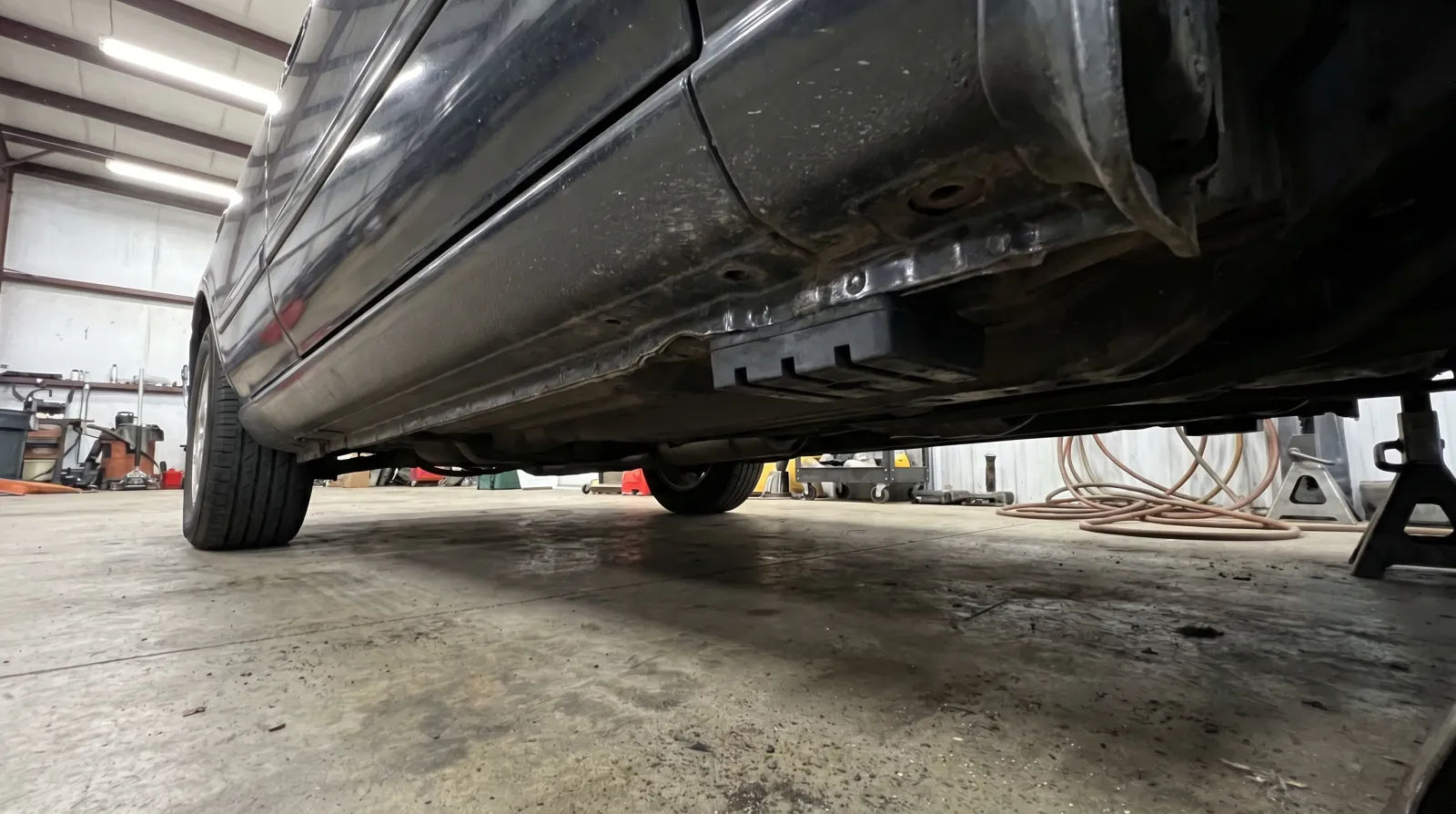 Underside view of a JDM sports car showing pinch weld flanges and front subframe cross-member highlighted with clean garage lighting