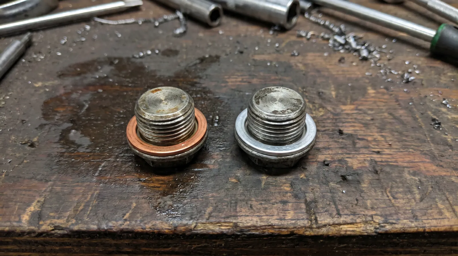 Two drain plugs side by side, one with a copper crush washer and one with an aluminium washer