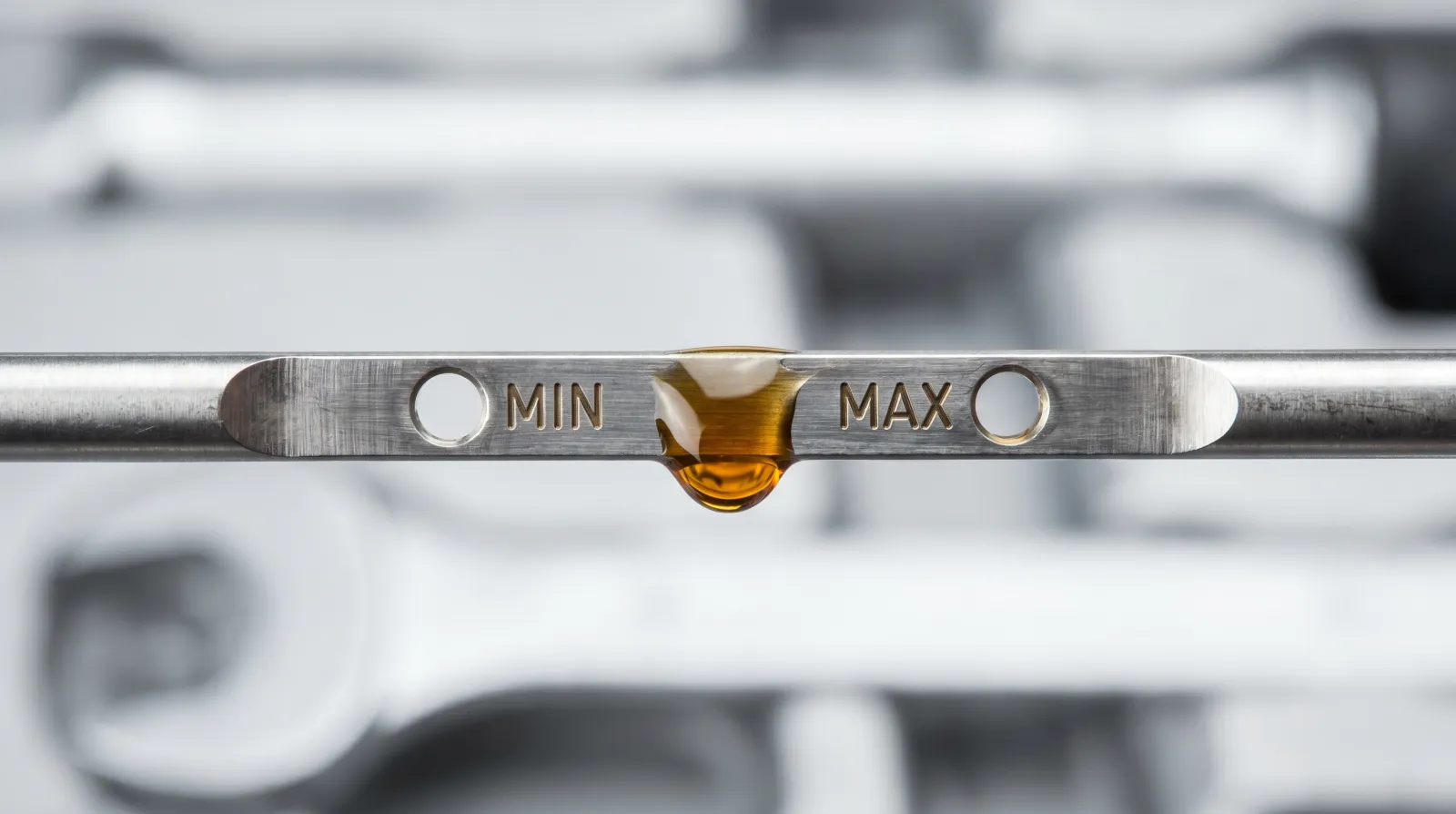 Macro of a dipstick held horizontally with the oil level sitting between the two punched min and max marks