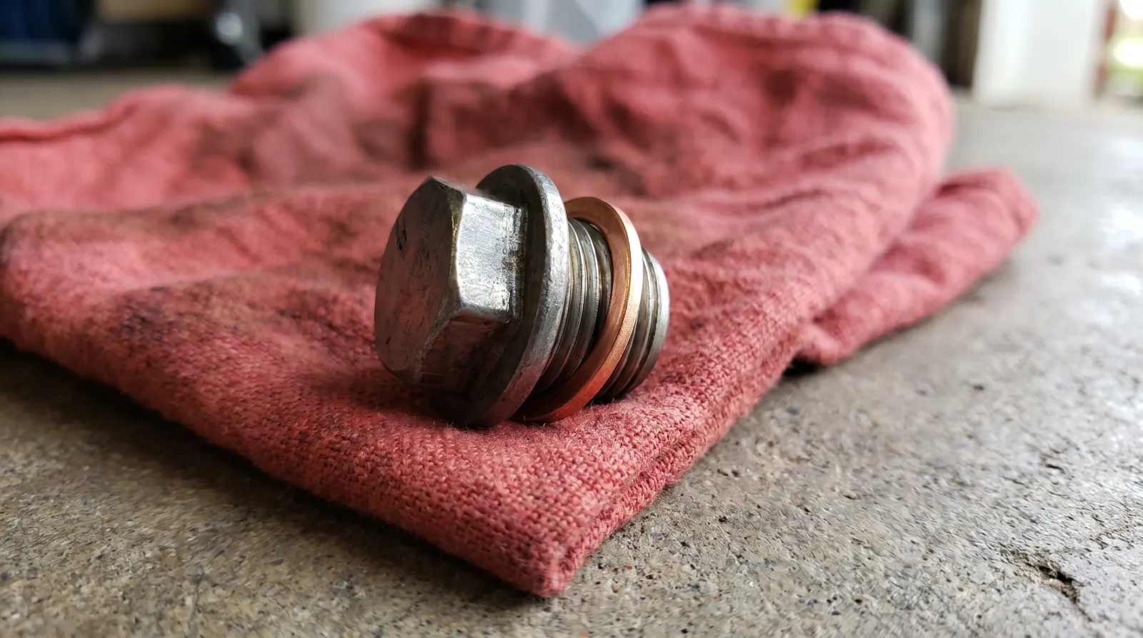 A clean sump drain plug with a new copper crush washer fitted, resting on a shop rag