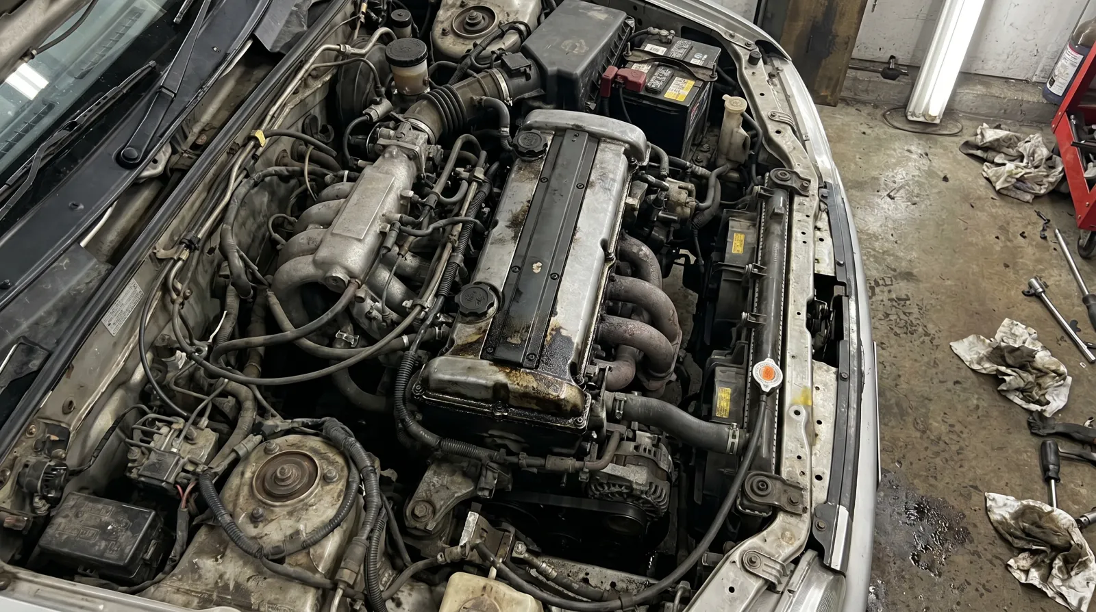 An older JDM 4-cylinder engine bay with visible oil residue around the valve cover